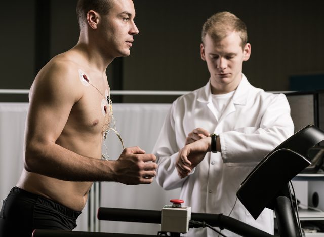 Man running on treadmill during medical test and medic in white uniform