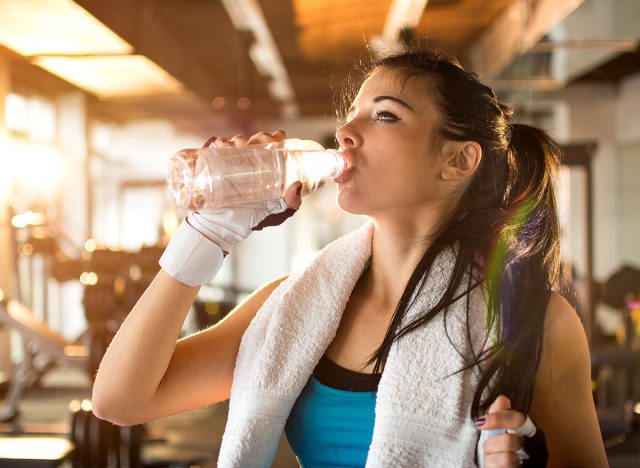 Young athletic woman drinking water in gym.