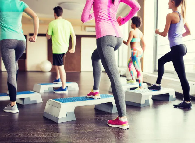 fitness, sport, training, aerobics and people concept - close up of people working out with steppers in gym from back