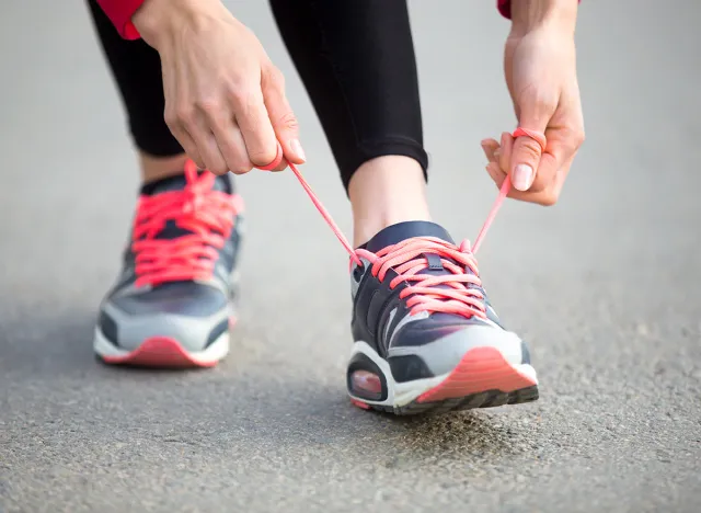 Female hands tying shoelace on running shoes before practice. Woman athlete preparing for jogging outdoors. Runner getting ready for training. Sport active lifestyle concept. Close-up