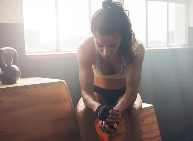 Young woman sitting on a box at gym after her workout and looking down. Female athlete taking rest after fitness training at gym.