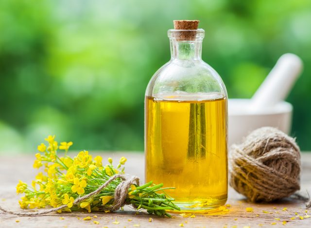 Bottle of rapeseed oil (canola) and rape flowers on table outdoors