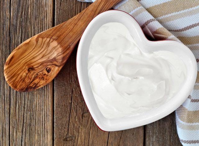 Greek yogurt in a heart shaped bowl, overhead scene against a rustic wood background