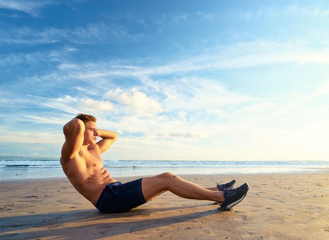 Sports and healthy lifestyle. Young man doing crunches on the ocean beach.