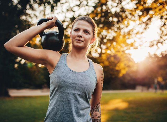 Portrait of fit young woman with kettlebell weights in the park. Fitness woman training with weights in park.
