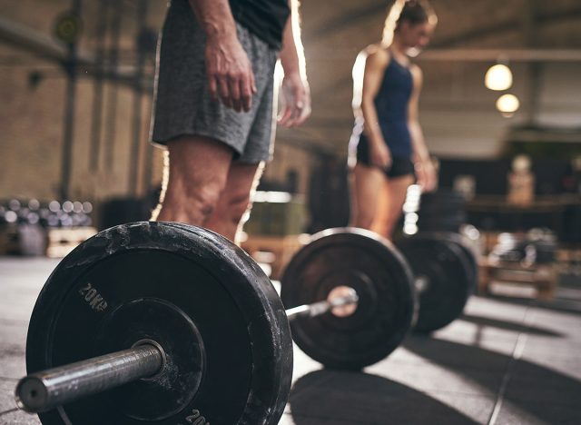 Fit people standing at barbells before exercise. Horizontal indoors shot