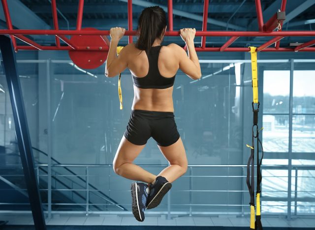 Athletic woman training on horizontal bar in gym pull ups