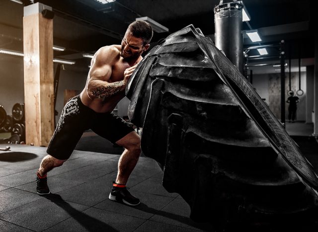 Shirtless man flipping heavy tire at gym