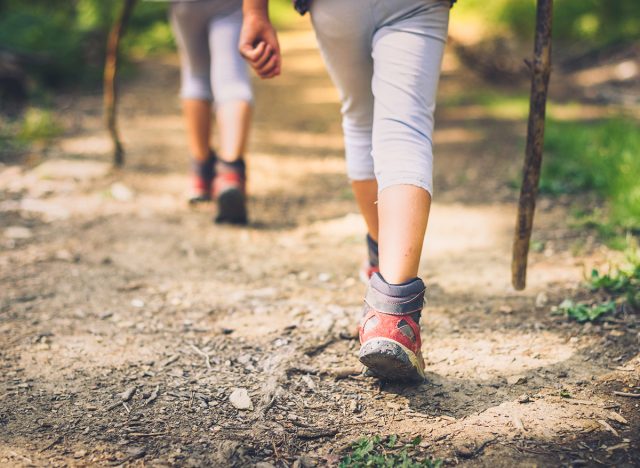 Children hiking in mountains or forest with sport hiking shoes. Girls or boys are walking trough forest path wearing mountain boots and walking sticks. Frog perspective with focus on the shoes.