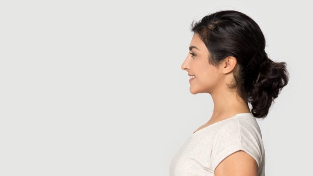 Side profile view smiling happy millennial Indian ethnicity girl standing on right, looking at empty space.