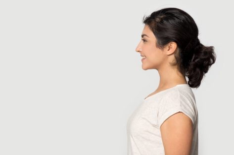 Side profile view smiling happy millennial Indian ethnicity girl standing on right, looking at empty space.