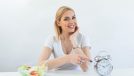 Dieting woman pointing on a clock wit salad on her side.