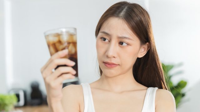 Young woman looking at a glass of soft drink soda with ice in her hand.