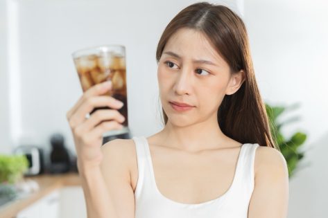 Young woman looking at a glass of soft drink soda with ice in her hand.