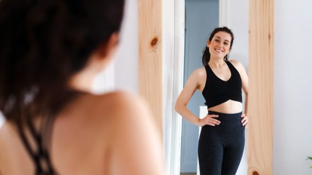 Young happy beautiful woman looking in the mirror satisfied with the results of her training.