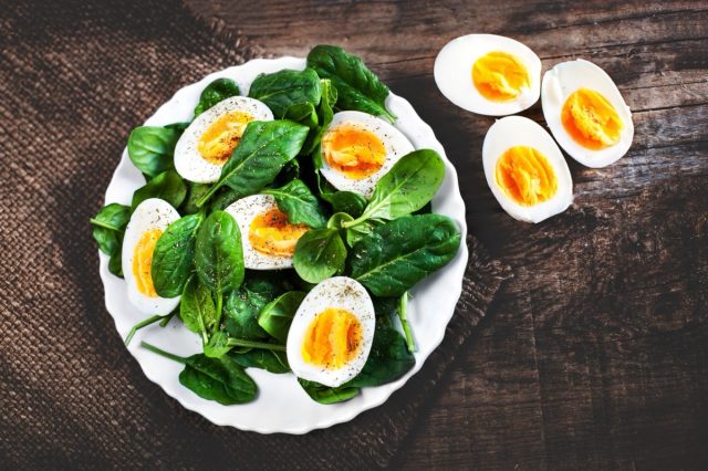 Healthy Salad - spinach baby leaves and boiled eggs cut in a half on wooden table.