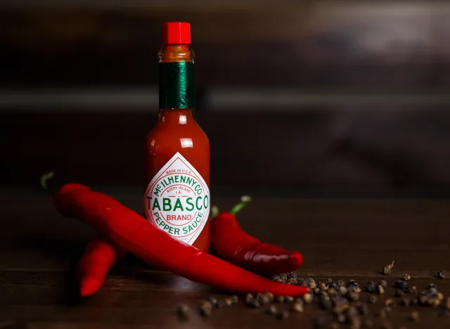 February 06, 2018, Belarus, Minsk. Horizontal photo of a tabasco sauce bottle with red chilli and black peppers, dark wooden background. Selective focus.