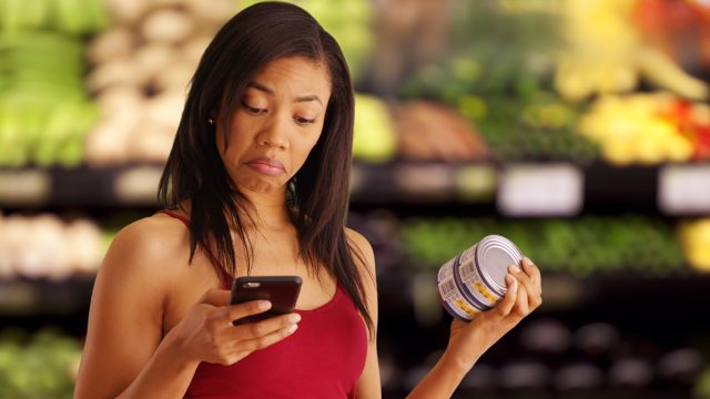 Pretty African-American millennial girl reading text while out grocery shopping