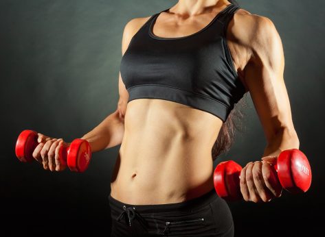 Body of a young fit woman lifting dumbbells on dark background