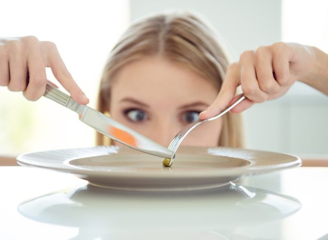 I'll eat you tiny pea! Weight loss concept. Close up photo portrait of mad lady's eye looking at small one pea on large big plate on table