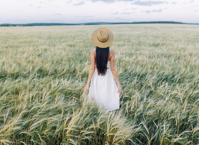 Girl walking on the field, in a hat and summer dress. Smiling and laughing, beautiful sunset in the forest and in nature. White dress and rye, sloping fields. Happy traveler, lifestyle.