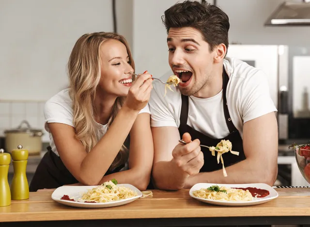 Image of happy excited young friends loving couple chefs on the kitchen eat tasty pasta.