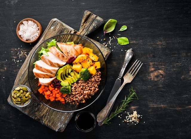 Bowl Buddha. Buckwheat, pumpkin, chicken fillet, avocado, carrots. On a black background. Top view. Free space for your text.