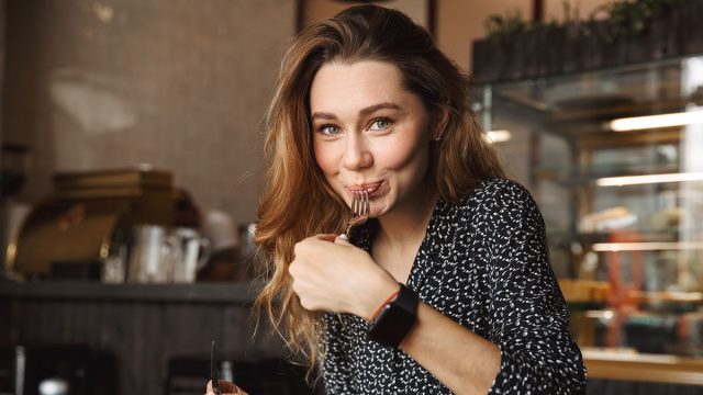 Photo of excited beautiful young pretty woman sitting in cafe indoors have a breakfast eating salad