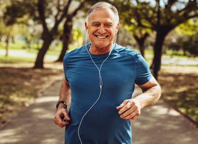 Portrait of a senior man in fitness wear running in a park. Close up of a smiling man running while listening to music using earphones.