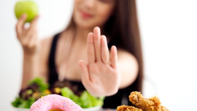 Young girl on dieting for good health concept. Close up female using hand reject junk food by pushing out her favorite sweet donuts and fried chicken and choose green apple and salad for good health.