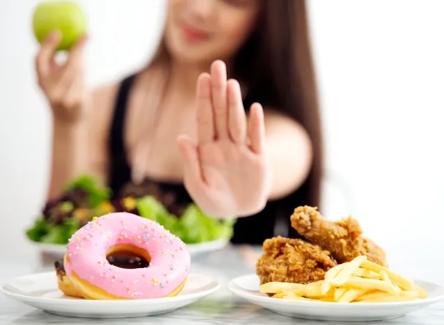 Young girl on dieting for good health concept. Close up female using hand reject junk food by pushing out her favorite sweet donuts and fried chicken and choose green apple and salad for good health.