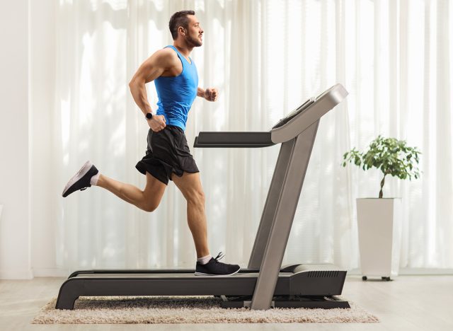 Full length profile shot of a young man running on a treadmill at home