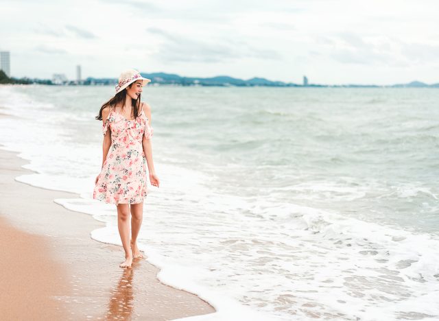Young asian tourist woman walk and relaxing on the beach. In pink dress cloth and hat during summer season holiday. Pattaya, Thailand