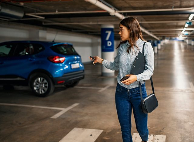 Woman in a parking garage, unlocking in her car. Woman activating her car alarm in an underground parking garage as she walks away. Business woman walking with car keys in the underground parking