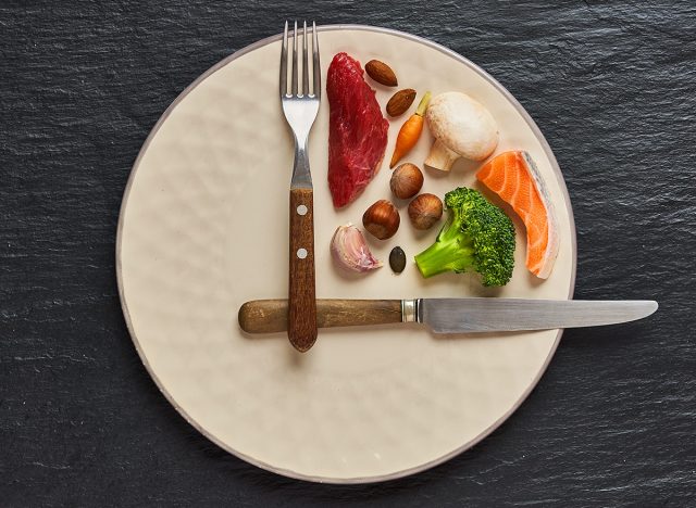 20:4 fasting diet concept. One third plate with healthy food and two third plate is empty. Beef, salmon, egg, broccoli, tomato, nuts, carrots, mushrooms. Dark background. Top view.