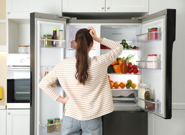 Young woman near open refrigerator in kitchen, back view