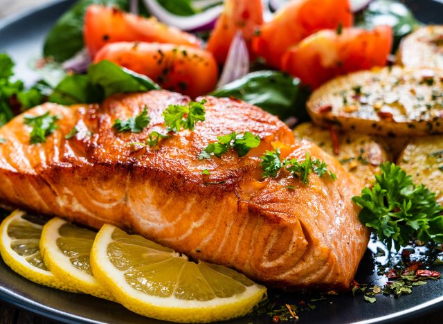 Fried salmon steak with potatoes and vegetables on wooden table