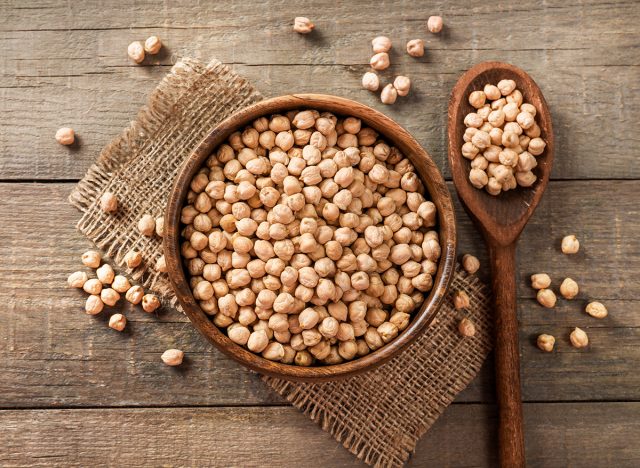 Wooden bowl and wooden spoon full of chickpeas on wooden background. Top view.