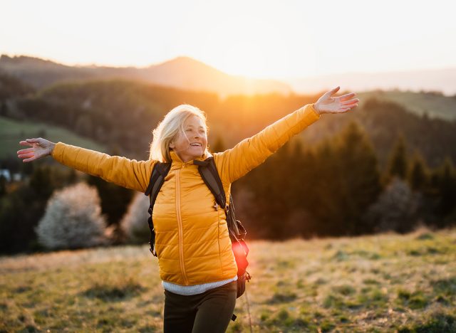 Front view of senior woman hiker standing outdoors in nature at sunset.