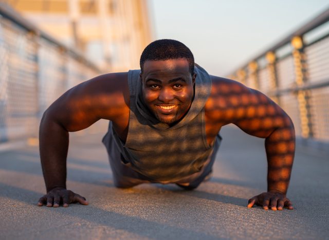 Young african-american man is exercising on the bridge in the city. He is doing push-ups.