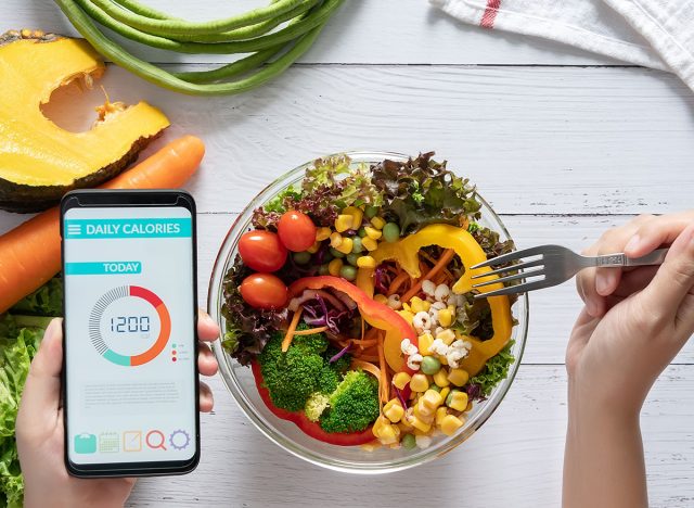 Calories counting , diet , food control and weight loss concept. Calorie counter application on smartphone screen at dining table with salad, fruit juice, bread and fresh vegetable. healthy eating