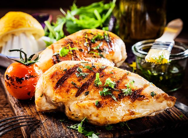 Marinated grilled healthy chicken breasts cooked on a summer BBQ and served with fresh herbs and lemon juice on a wooden board, close up view