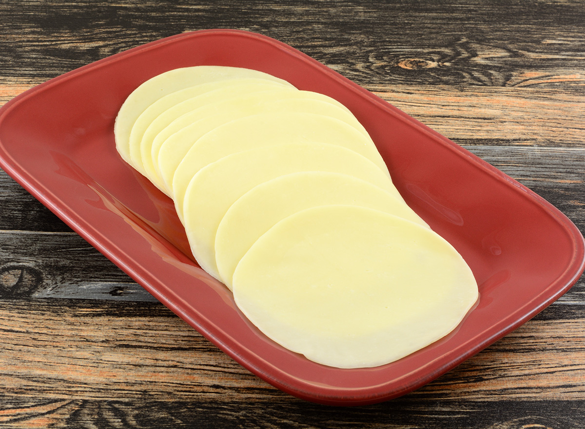 Provolone cold cut cheese slices on red serving platter on table