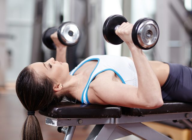 Young woman bench pressing with dumbbells in the gym, working triceps and chest