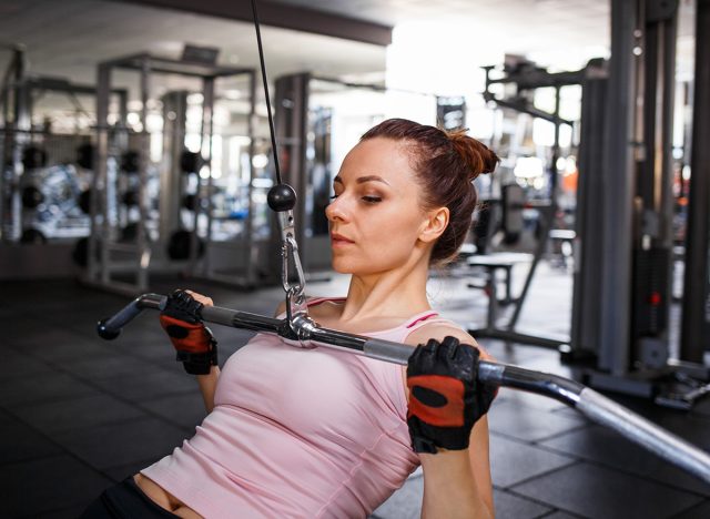 Young sporty woman training her lats and biceps on cable machine in gym