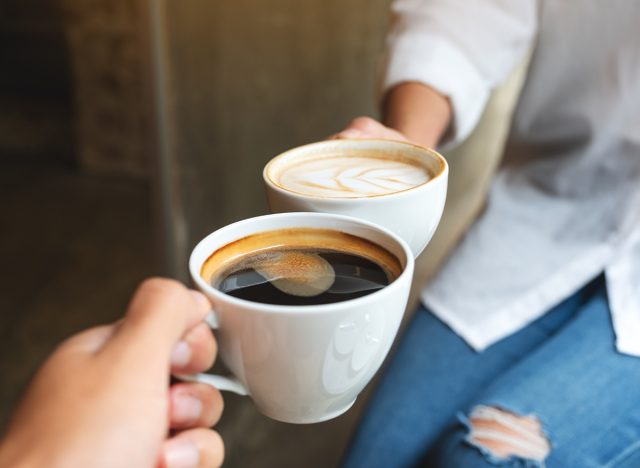 Closeup image of man and woman clinking white coffee mugs in cafe