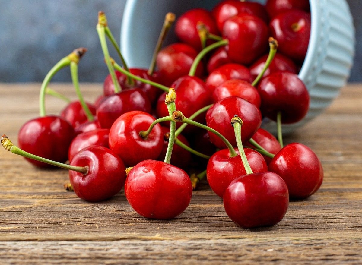 Ripe wet sweet cherries are poured out of the blue bowl on wooden background