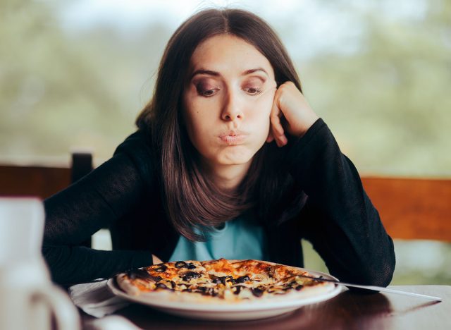 Sad Woman Looking at the Pizza in Her Plate. Female obsessing over counting calories thinking about eating fast-food