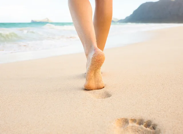 Beach travel - woman walking on sand beach leaving footprints in the sand. Closeup detail of female feet and golden sand on Maui, Hawaii, USA.