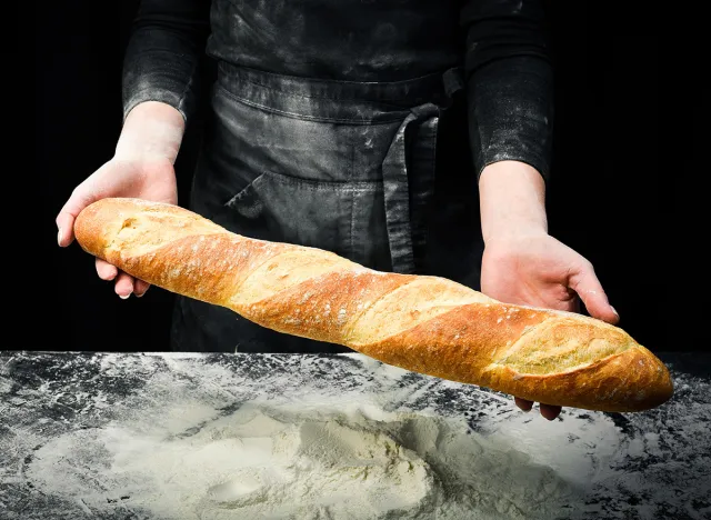 Fragrant fresh baguette in hands. Black cooking background. Isolated on black background.
